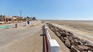 Una carretera costera con baranda de seguridad, acera pavimentada y una playa al fondo.