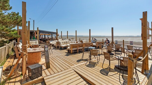 Una terraza de madera con asientos exteriores, un área techada y vista a la playa.