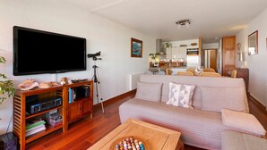 Una sala de estar con televisor de pantalla plana, mueble de madera para entretenimiento, sofá y una mesa de centro.