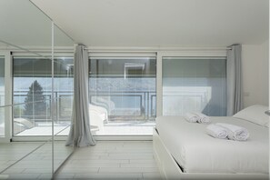A modern hotel room with a large bed, a glass partition, and a view of the city. - Open View Apartment by Wonderful Italy (Oliveto Lario)