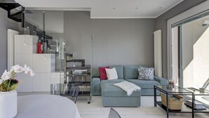 Ein zeitgemäßer Wohnraum mit einer Couch, einem Glastisch und einer Treppe, die in ein Obergeschoss führt.