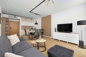 Ein modernes Wohnzimmer mit einer Couch, einem Couchtisch, einem Fernseher und einem Essbereich mit Stühlen und einem Tisch.