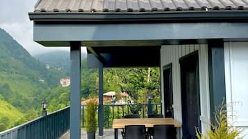 A covered outdoor seating area with a table and chairs, overlooking a mountainous landscape.