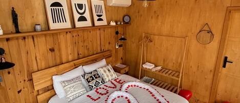 Une chambre à coucher aux murs lambrés, avec un lit, des tables de chevet, un luminaire suspendu et un climatiseur fixé au mur.