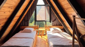 A triangular attic bedroom with two beds, a window, and a view of the outside.