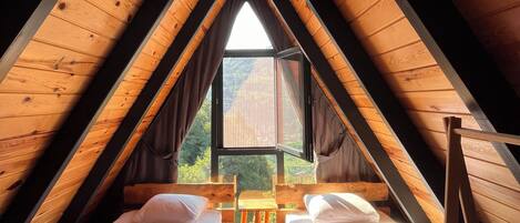 Dormitorio en ático triangular con dos camas, una ventana y vistas al exterior.