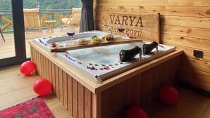 A wooden room with a hot tub, a wooden ceiling, and a view of green hills.