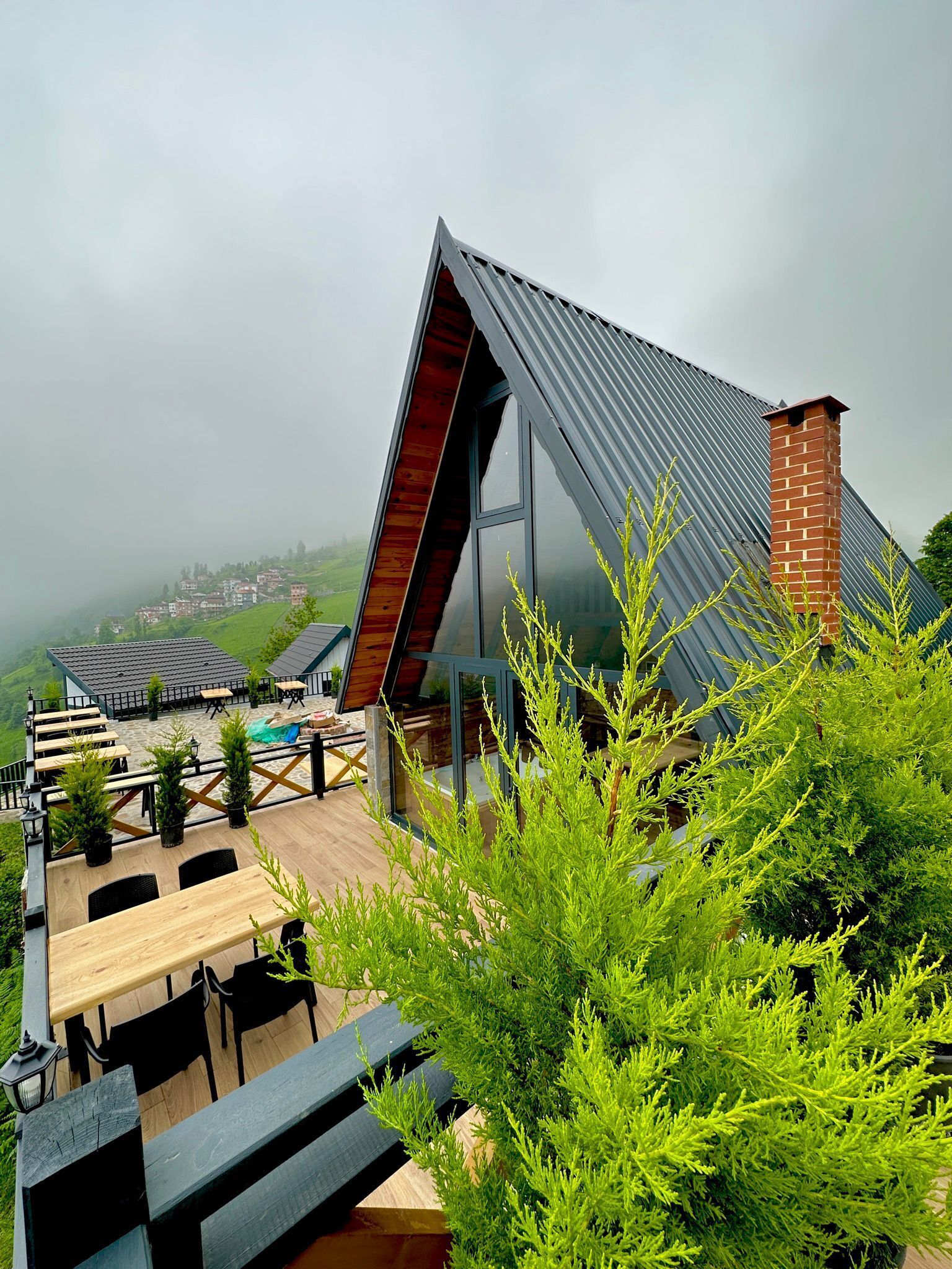 A modern building with a sloped roof, outdoor seating area, and a view of a hilly landscape.