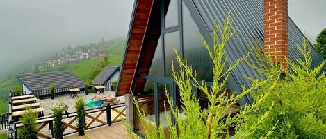 A modern building with a sloped roof, outdoor seating area, and a view of a hilly landscape.