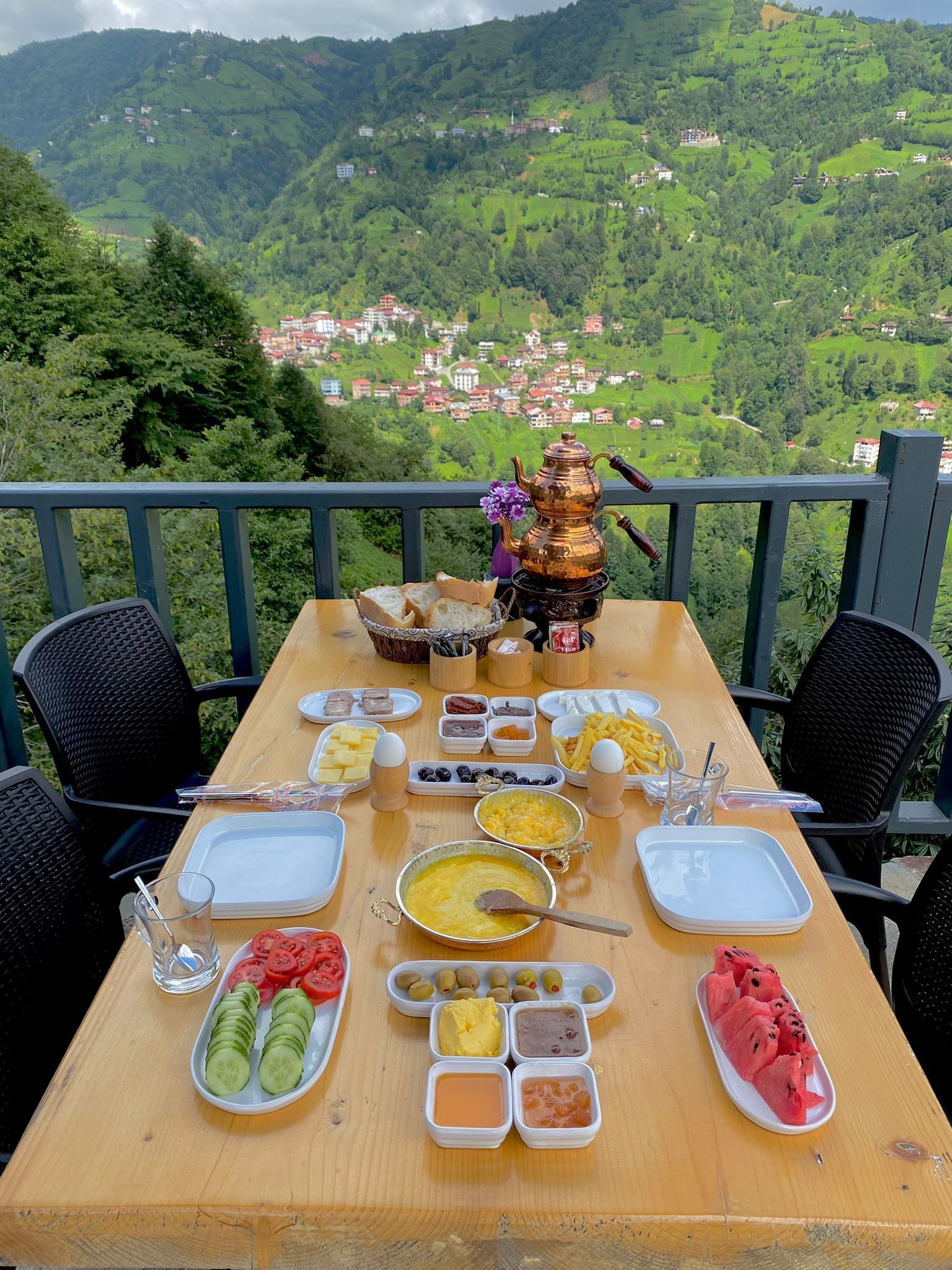 A table set with food and a teapot on a balcony overlooking a mountainous landscape.