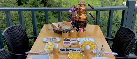 A table set with food and a teapot on a balcony overlooking a mountainous landscape.