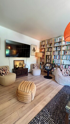 A living room with a flat-screen TV, bookshelves, a round ottoman, and a patterned rug. - Villa les Lézards: Set on a private lot with a pool, not overlooked by neighbors (Bagard)