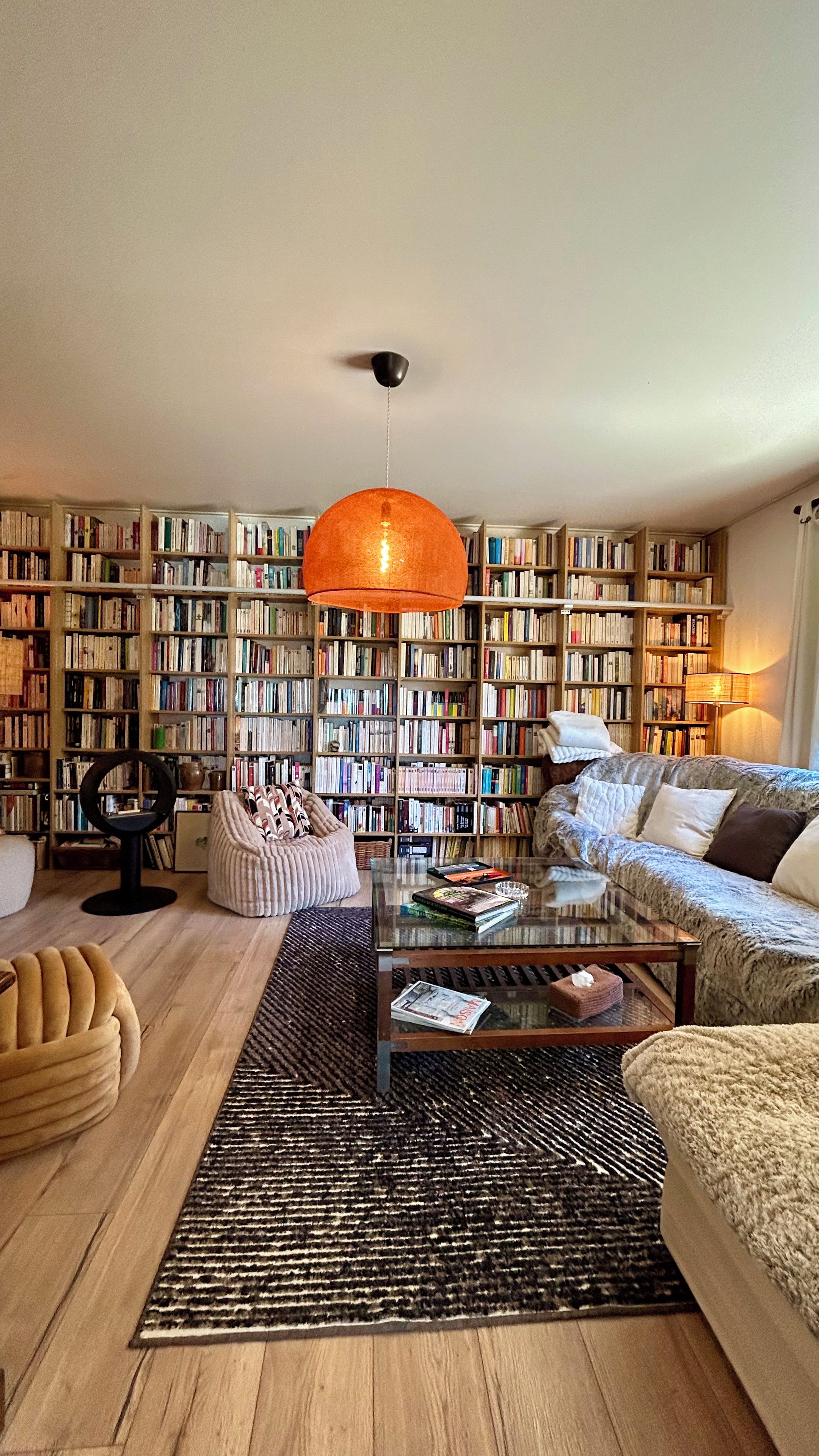 A living room with a large bookshelf, a round orange light fixture, a glass coffee table, and a sofa.