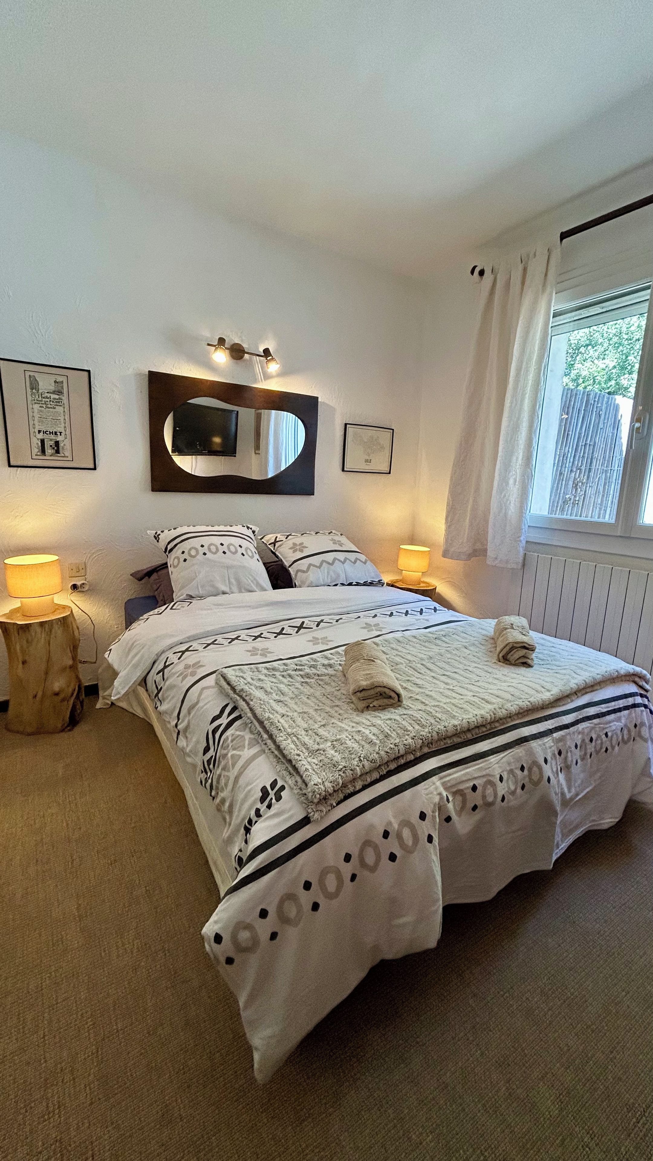 A bedroom with a bed, bedside lamps, a mirror, and a window with curtains.