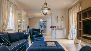 A living room with a blue sofa, ottoman, and armchair, a chandelier, and a television. - Villa Cesara - Casa del Sole (Tar-Vabriga)