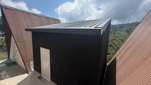 Un edificio pequeño y oscuro con techo inclinado, rodeado de otros edificios con techos similares.