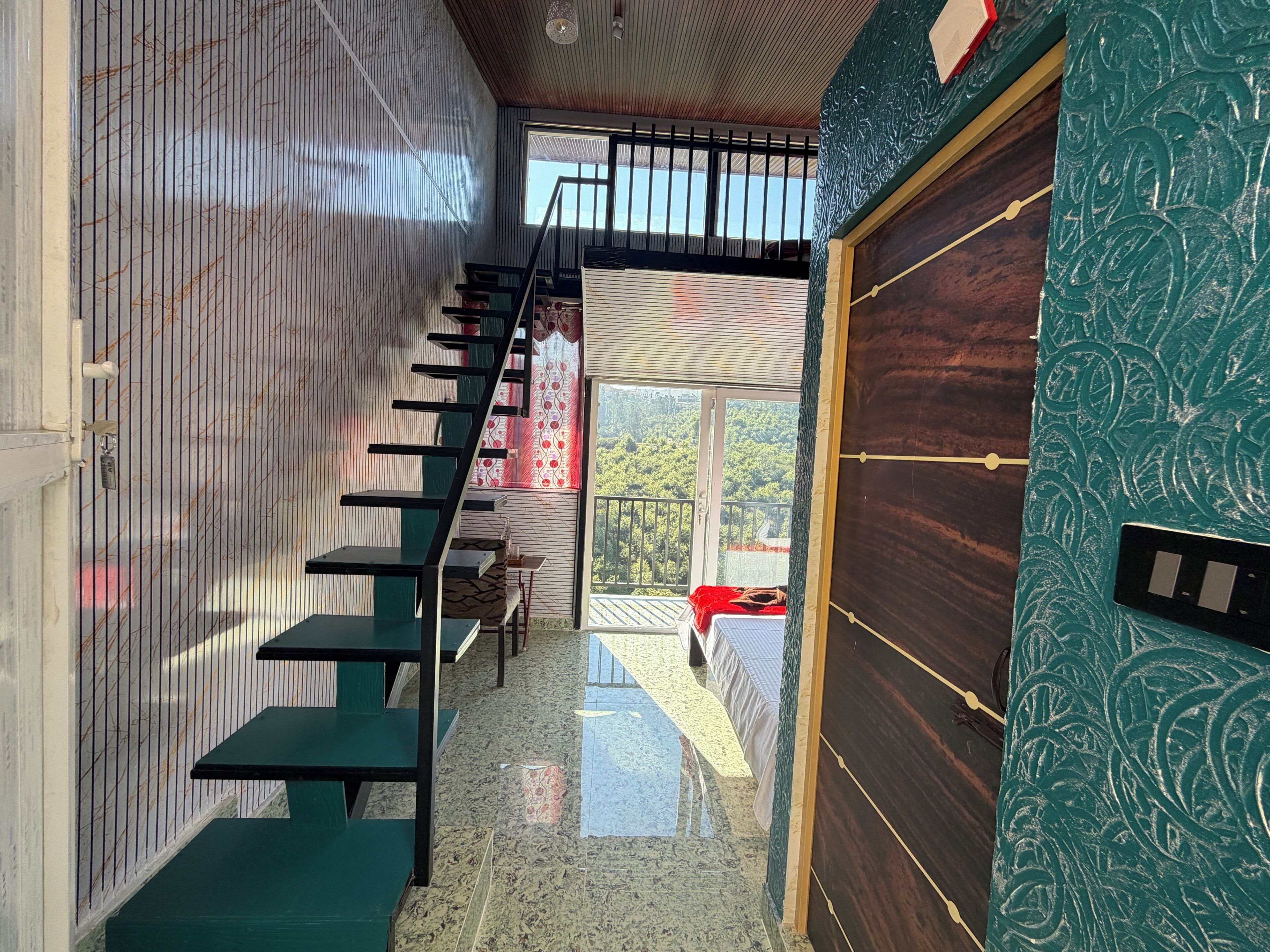 A staircase leading to a balcony with a view of greenery, a door with a decorative pattern, and a small table with a red cloth.