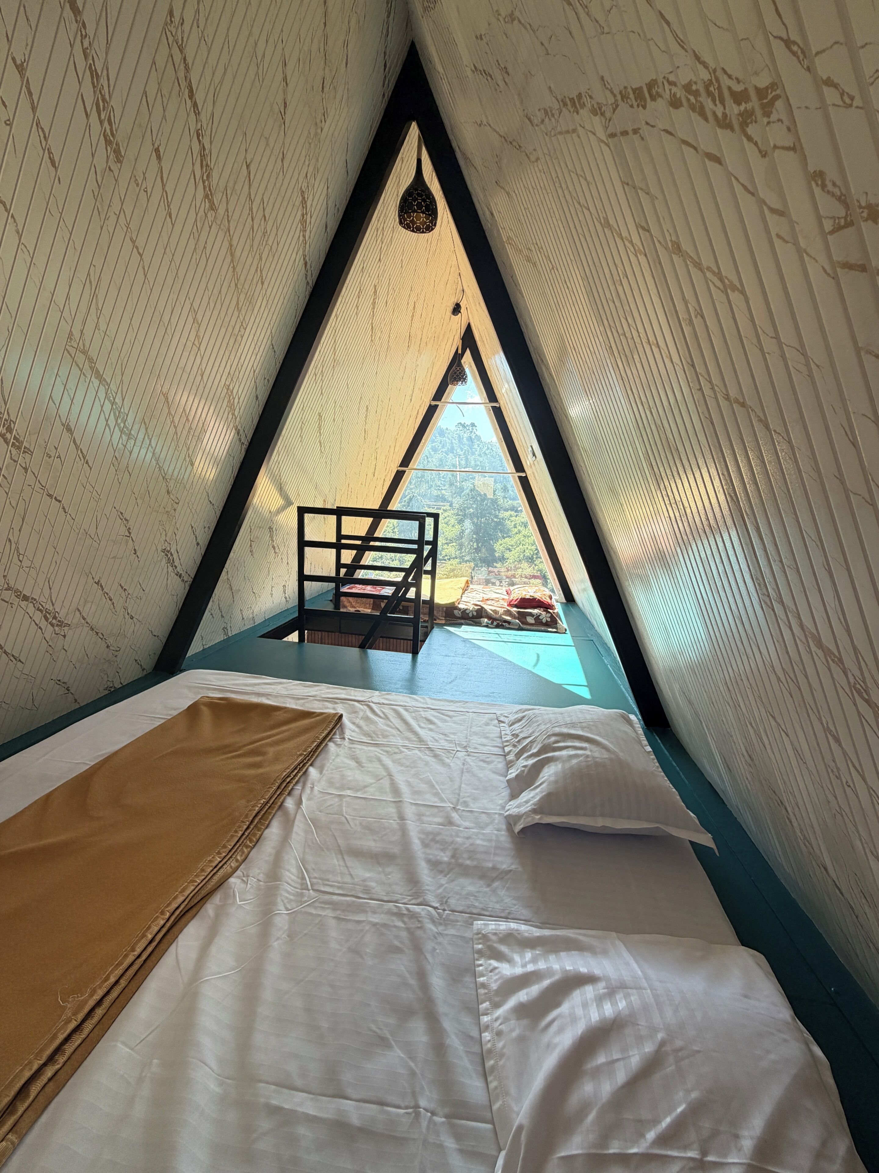 Una habitación triangular con una cama, una escalera de madera y vistas al exterior.