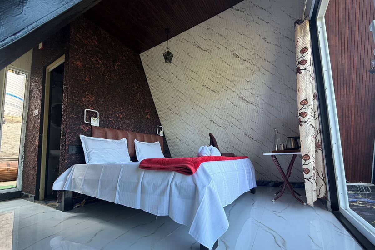 Um quarto com cama, mesa de cabeceira, luminária, janela e porta.