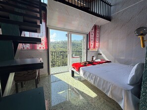 Una habitación con cama, escritorio, balcón con vistas al bosque y pared con diseño.