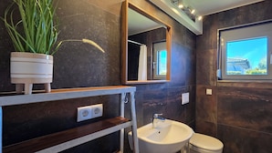 A modern bathroom with a large mirror, a sink, a toilet, and a window with a view. - Bungalow for 2 people with one bedroom, approx. 400 m to the beach (Graal-Müritz)
