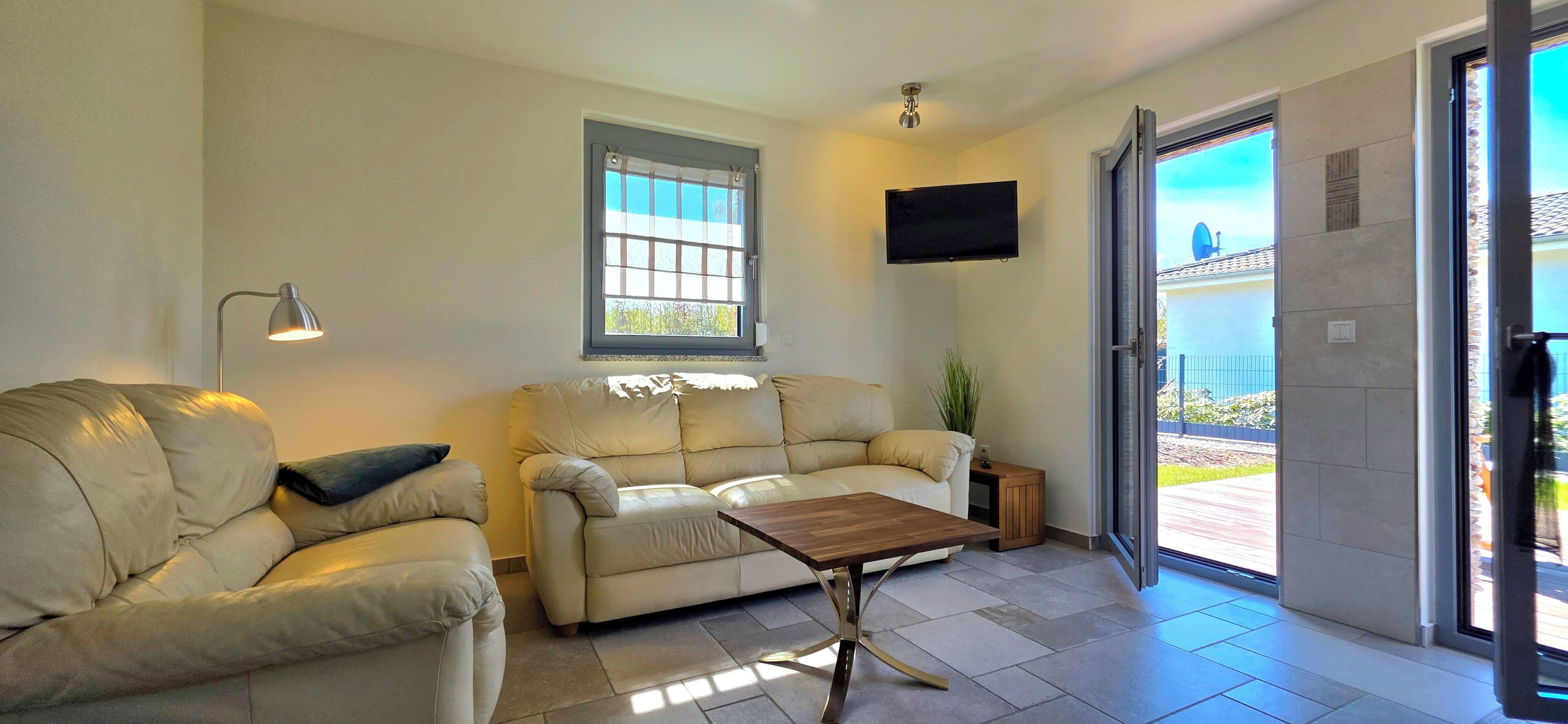 Una sala de estar con dos sofás, una mesa de centro, un televisor, una ventana y una puerta que da al exterior.
