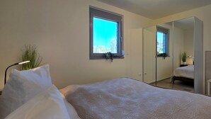 A bedroom with a bed, a window, a mirror, and a bedside plant. - Bungalow for 2 people with one bedroom, approx. 400 m to the beach (Graal-Müritz)