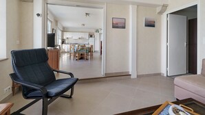 Ein Wohnzimmer mit einem schwarzen Sessel, einer rosa Couch und einem Essbereich mit Tisch und Stühlen.