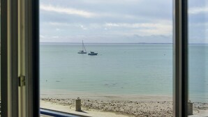 Blick auf ein ruhiges Meer mit zwei ankernden Booten, einen Sandstrand und einen bewölkten Himmel.