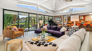 Een ruime woonkamer met een grote glazen deur naar een terras, een vleugelpiano en een moderne keuken met oranje accenten.