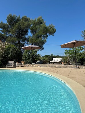 A swimming pool with lounge chairs and umbrellas, surrounded by trees and a stone wall. - Villa les Oliviers and its beautiful pool (Bagard)