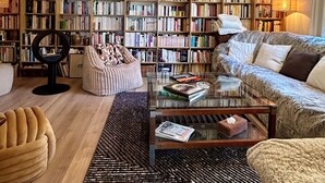 A living room with a large bookshelf, a round orange light fixture, a glass coffee table, and a sofa. - The Villa des OLiviers and its superb swimming pool (Bagard)