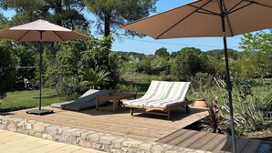 An outdoor patio with a wooden deck, two beige umbrellas, a lounge chair, and a table. - The Villa des OLiviers and its superb swimming pool (Bagard)