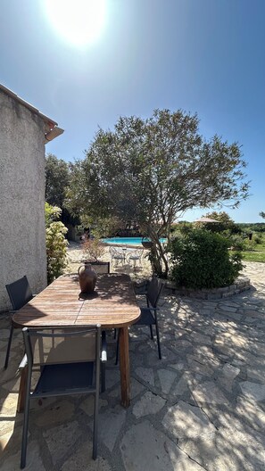 An outdoor patio with a wooden table and chairs, a stone pathway, and a swimming pool in the background. - Villa les Oliviers and its beautiful pool (Bagard)