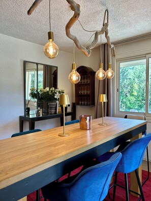 A dining area with a wooden table, blue chairs, hanging light fixtures, and a large mirror.