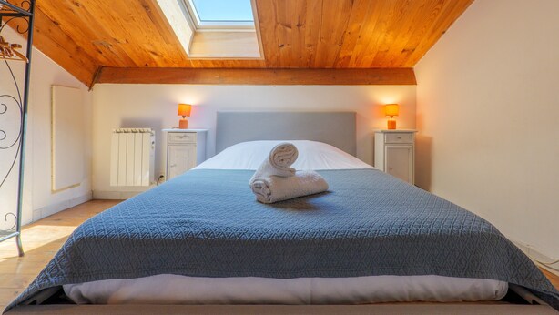 Una camera da letto con un velux, un letto con asciugamano arrotolato, due comodini con lampade e un termosifone.
