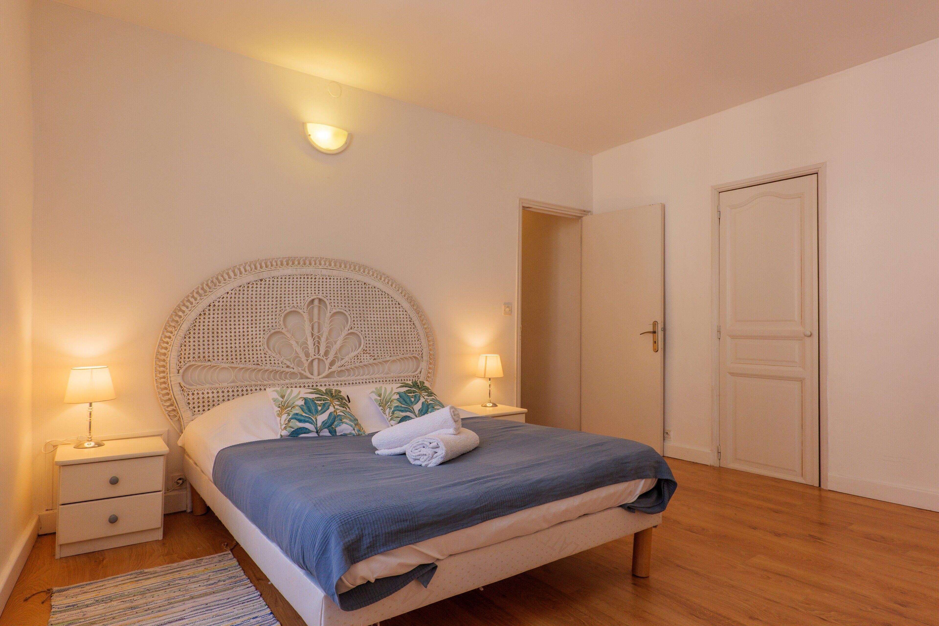 Une chambre à coucher comprenant un lit, des lampes de chevet, une table de chevet, une porte et un luminaire fixé au mur.