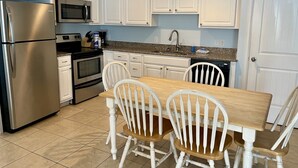 Una cocina con armarios blancos, un refrigerador de acero inoxidable, un microondas, un horno, un fregadero y una mesa de comedor con cuatro sillas.