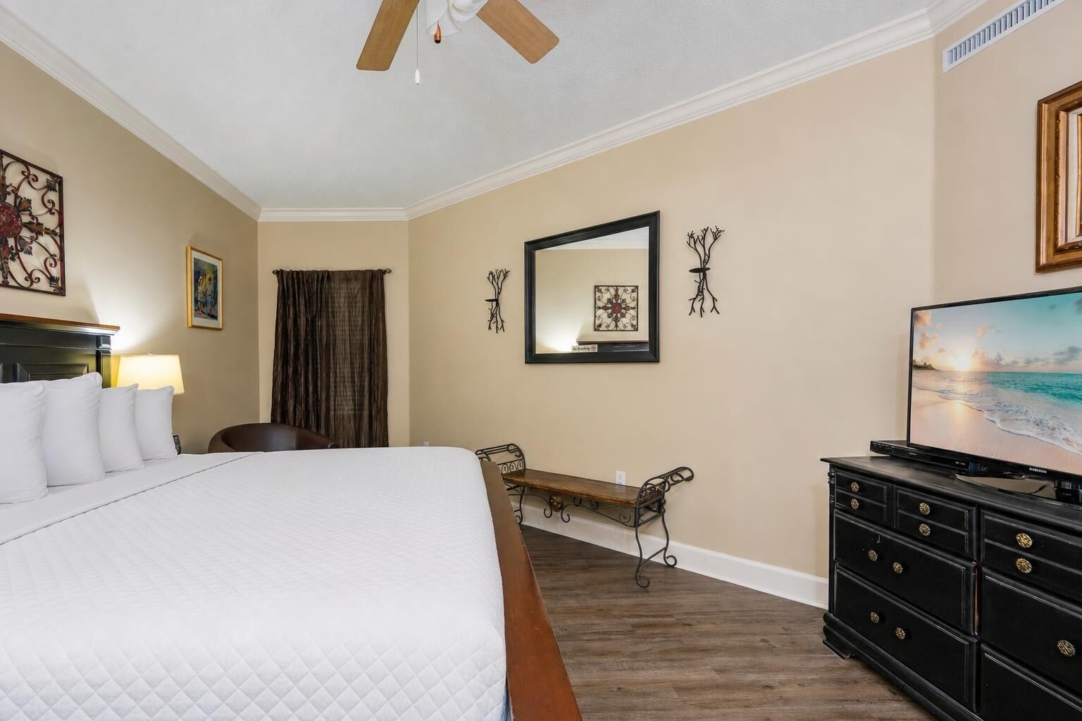 A hotel room with a bed, a desk, a television, and a ceiling fan.
