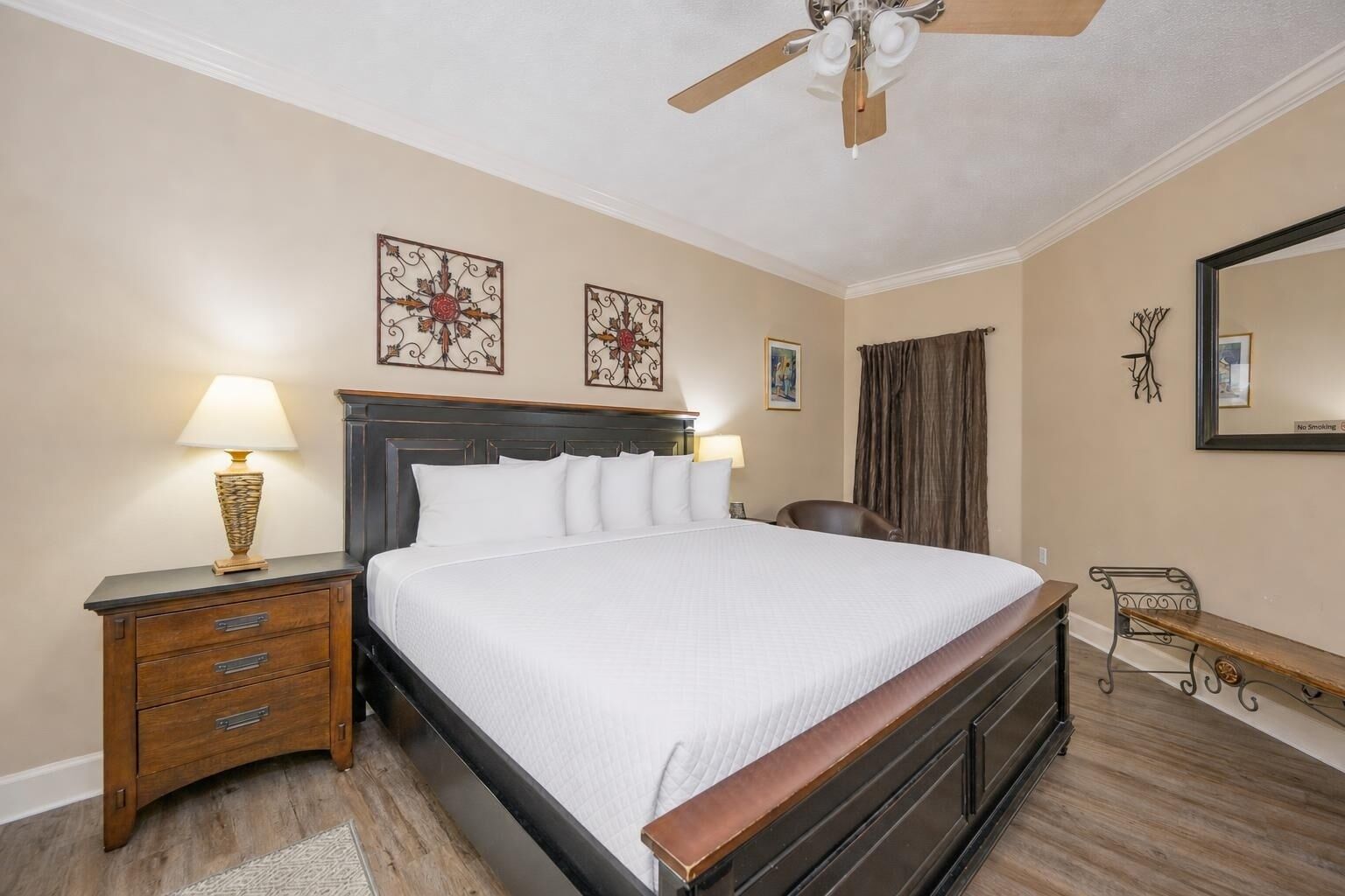 A hotel room with a bed, a nightstand with a lamp, a ceiling fan, and artwork on the walls.