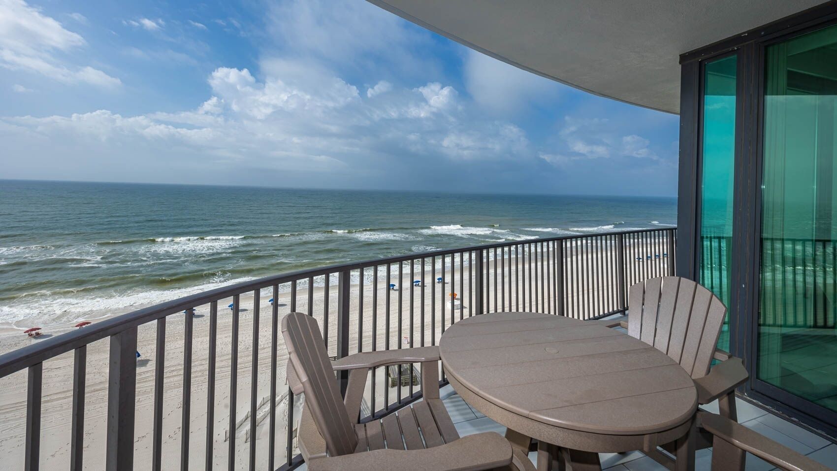 A balcony with a table and chairs overlooking the beach and ocean.