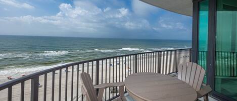 Ein Balkon mit Tisch und Stühlen mit Blick auf Strand und Meer.