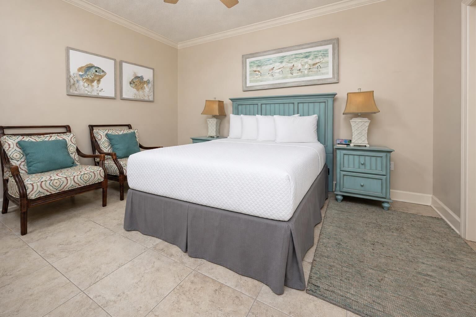 A bedroom with a bed, two chairs, a nightstand, and wall art.