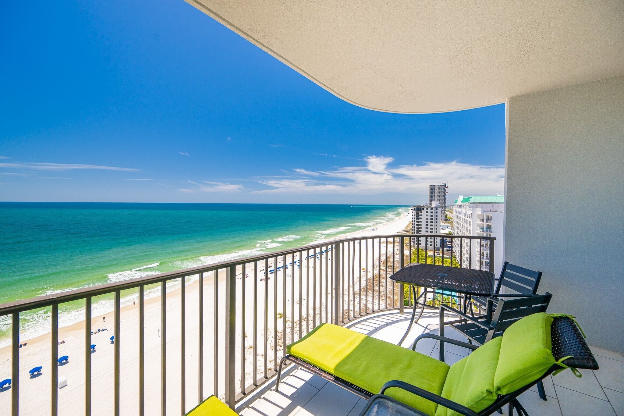 Een balkon met uitzicht op het strand en de oceaan, een tafel, stoelen en een zonnescherm.