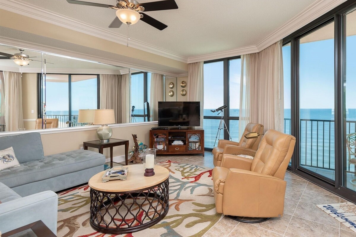 A spacious living room with a sofa, armchairs, a coffee table, a TV, and a balcony with a view of the sea.