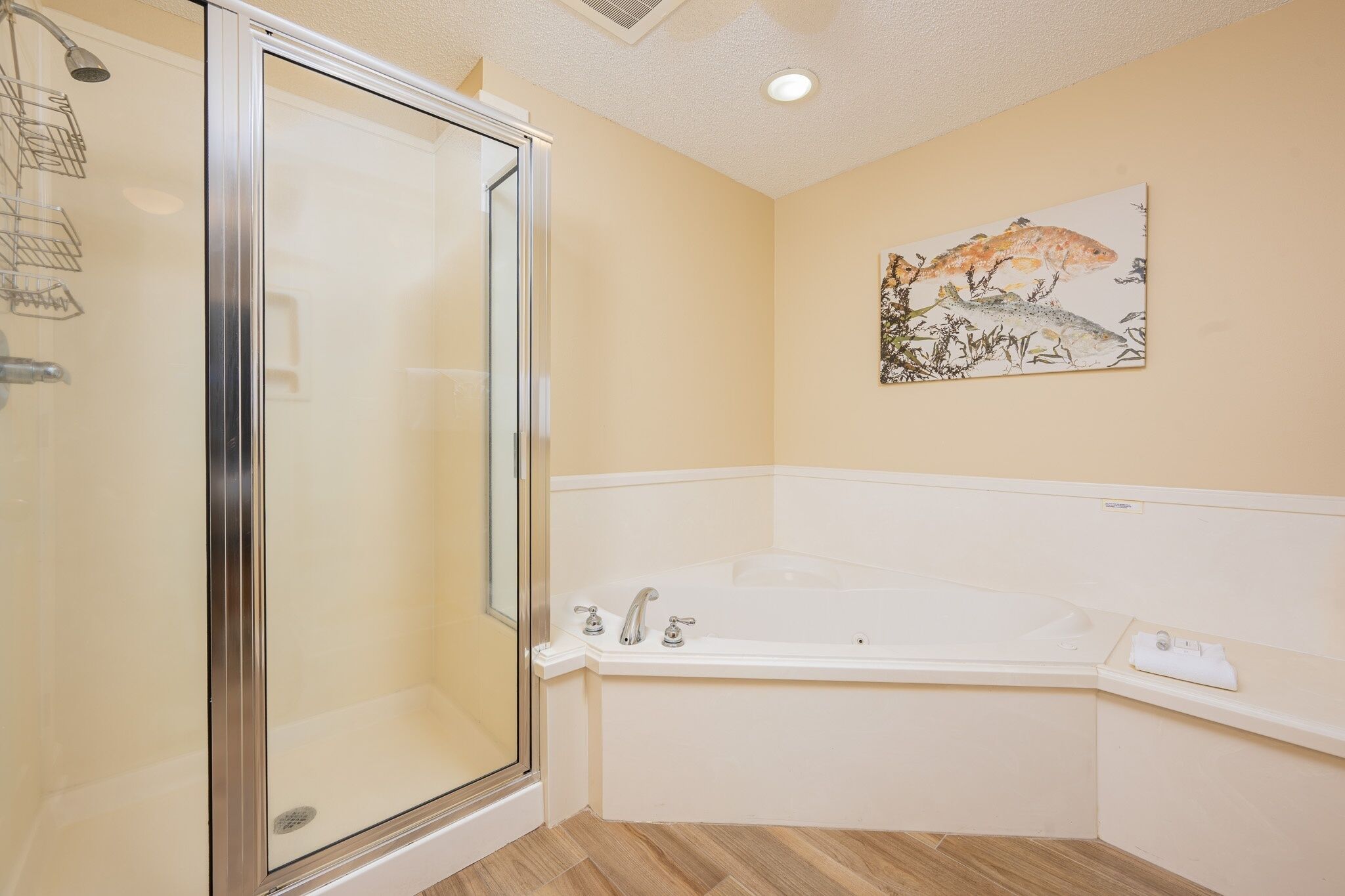A bathroom with a glass-enclosed shower, a white bathtub, and a wall-mounted artwork.