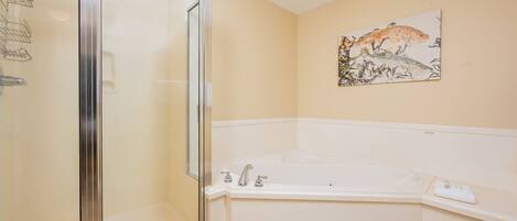 A bathroom with a glass-enclosed shower, a white bathtub, and a wall-mounted artwork.