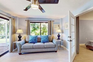 A living room with a sofa, two side tables with lamps, a ceiling fan, and a door leading to another room. - Waterfront home with private pool, kayaks, hot tub, bicycles, & W/D (Bonita Springs)