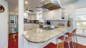 Uma cozinha moderna com armários brancos, bancada de granito, eletrodomésticos de aço inoxidável e uma ilha grande com banquetas.