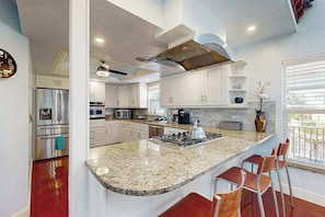 A modern kitchen with white cabinets, a granite countertop, stainless steel appliances, and a large island with bar stools. - Waterfront home with private pool, kayaks, hot tub, bicycles, & W/D (Bonita Springs)